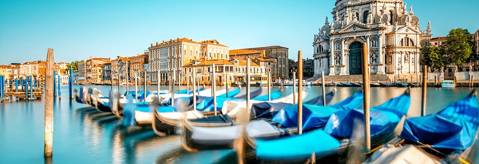 Fotografiet framställer gondoler som vaggar på lugnt vatten i Venedig, med historiska byggnader i bakgrunden.