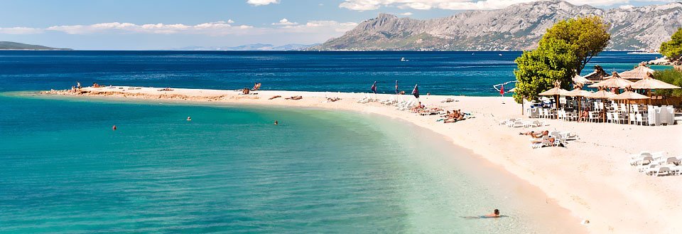 En pittoresk strandvy med klarblått vatten, vita sandstränder och berg i bakgrunden.