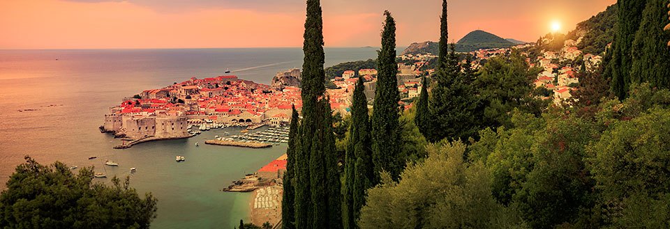 Fotot skildrar en stämningsfull solnedgång över Dubrovnik med röda tak och cypresser.