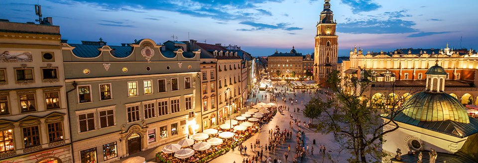 En myllrande torg i Krakow i skymningen med historiska byggnader, folkmassor och uteserveringar.