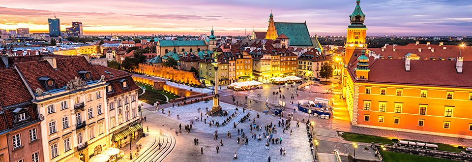 Fotot visar en kvällsbild av ett pittoreskt torg i Warszawa omgivet av gammaldags byggnader och promenerande folk.