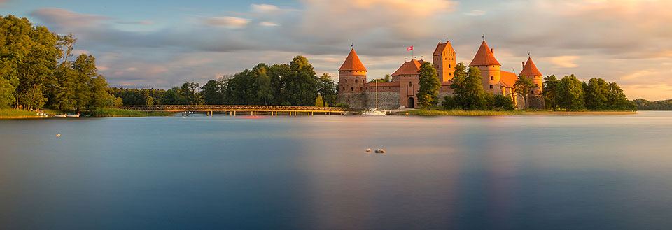 Bilden visar ett vackert slott vid vattenkanten omgivet av träd i skymningen.