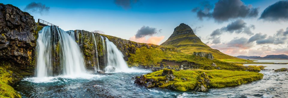 Panoramavy över ett majestätiskt isländskt vattenfall och ett konformat berg i bakgrunden vid solnedgången.