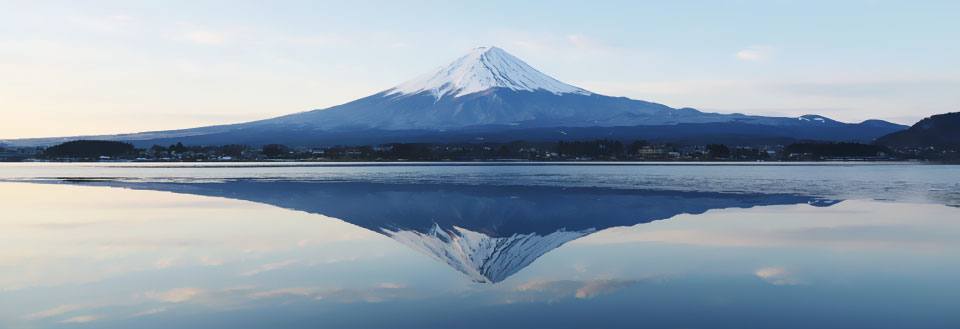 Bilden visar det snötäckta Mount Fuji speglat i vatten vid skymning.