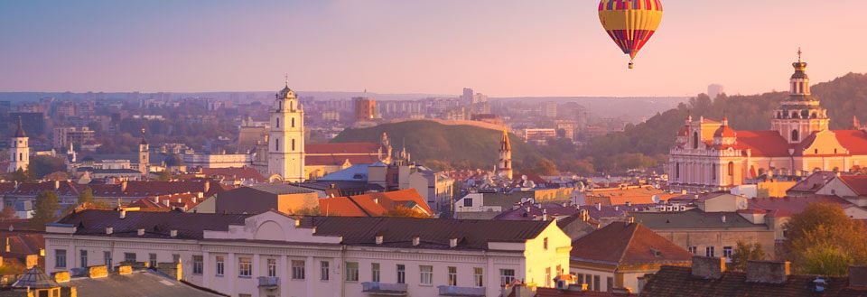 Vilnius vid solnedgången med kyrkor, gamla byggnader och en luftballong i skyn.