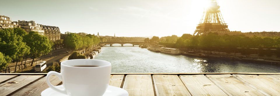 En vit kaffekopp på ett träbord med utsikt över Seine och Eiffeltornet i Paris.