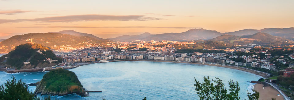 San Sebastian vid solnedgång med berg i bakgrunden och en bågformad strand i förgrunden.