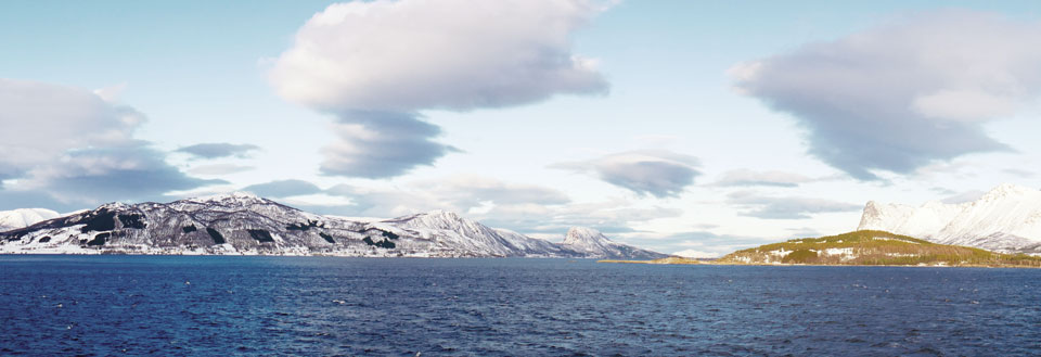 Vinterkust med snötäckta berg och delvis molnig himmel.