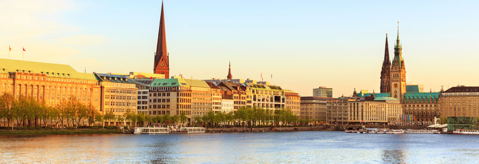 Bilden visar en panoramavy över en flodstrand med moderna byggnader och historiska kyrktorn.