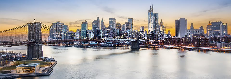 Panoramabild av New York i skymningen med en berömd bro och upplysta skyskrapor.