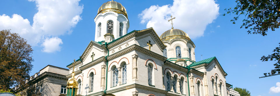 En ståtlig kyrka med gyllene kupoler och vit fasad mot en blå himmel.