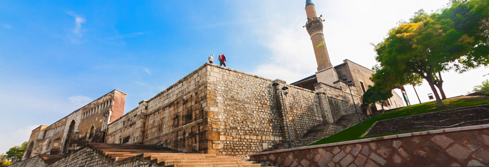 Historisk byggnad med en minaret, höga stenmurar och människor som njuter av utsikten.