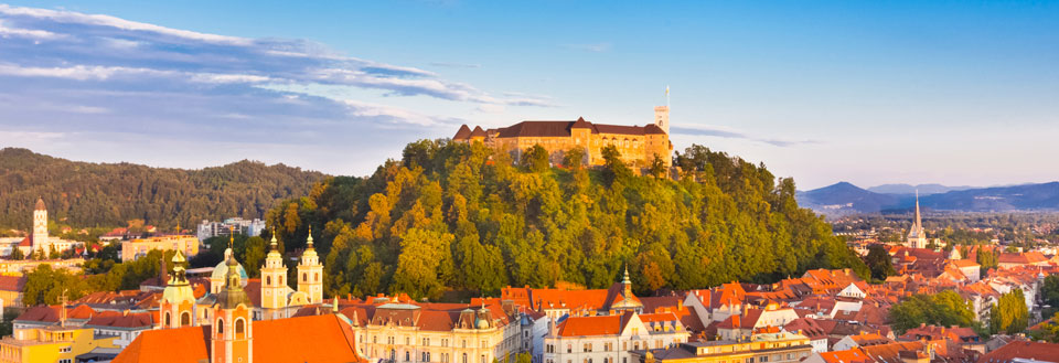 Europeisk stad i solnedgången, med historiska byggnader och ett slott på en kulle.