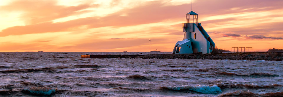 Ett fyrtorn vid havet under en färgrik solnedgång med upprörda vågor.