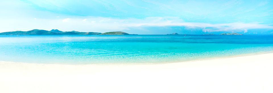 En pittoresk strand med klarblått hav och en himmel samt avlägsna öar.