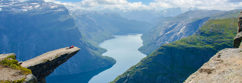 En person ligger på Trolltunga med benen utsträckta över en magnifik fjord.