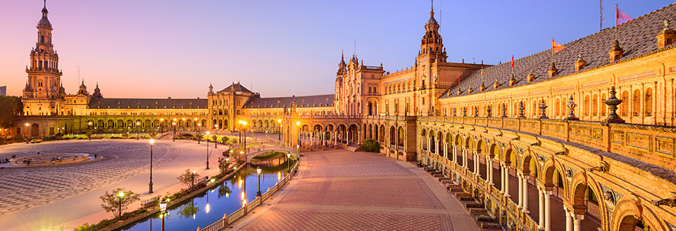 Plaza de España i Sevilla i skymningen, belyst, med vattenspegling och magnifik arkitektur.