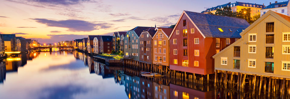 Färgglada trähus speglas i vattnet i skymningen i Trondheim.