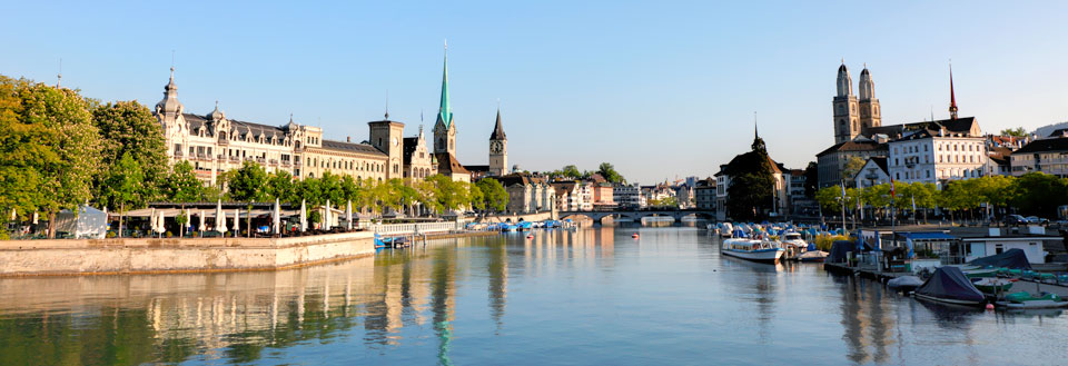 En panoramavy över en lugn flod i en europeisk stad med båtar, byggnader och kyrkor.