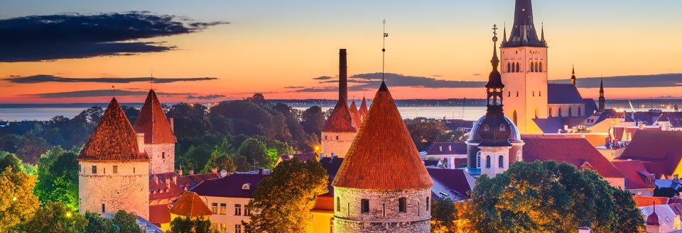 Solnedgång över en gammal stad med spiror och torn mot en färgrik himmel.