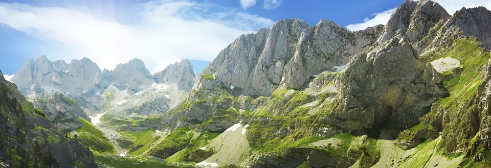 En majestätisk bergskedja med skarpa toppar och gröna dalar under en klarblå himmel.